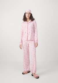 Rosa pyjamaset med röda hjärtan, som har en långärmad knäppblus och matchande byxor, kompletterat med en rosa sovmask och fluffiga tofflor.