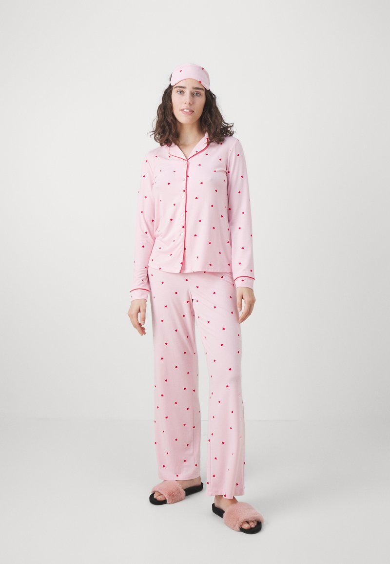 Rosa pyjamaset med röda hjärtan, som har en långärmad knäppblus och matchande byxor, kompletterat med en rosa sovmask och fluffiga tofflor.