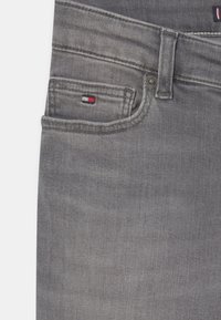 Jeans de mezclilla gris con un bolsillo delantero que cuenta con un pequeño parche de logo tricolor, costura visible y un diseño clásico de cinco bolsillos.