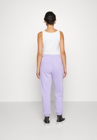 Lilac sweatpants in soft fabric with tapered legs, elastic waistband, and cuffed ankles, paired with a white tank top and black high-top sneakers.