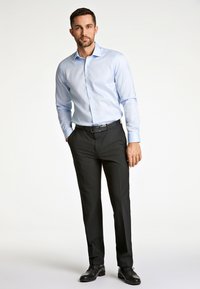 Lichtblauw knopshirt met een kraag, gecombineerd met zwarte broeken en zwarte schoenen. De outfit heeft een getailleerde pasvorm en een zachte textuur.