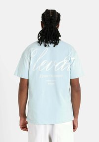 Camiseta de algodón azul claro de manga corta, con texto blanco en la parte posterior: "Eleva Cada Momento Desde 2008 Sixth June."