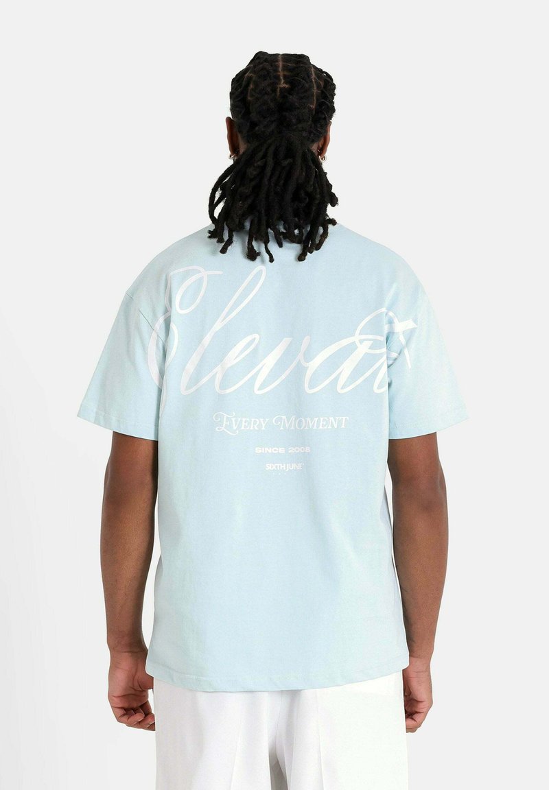 Camiseta de algodón azul claro de manga corta, con texto blanco en la parte posterior: "Eleva Cada Momento Desde 2008 Sixth June."