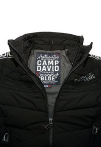Schwarze gesteppte Jacke mit vorderem Reißverschluss, zwei Reißverschluss-Brusttaschen, gebrandetes CAMP DAVID-Label innen sowie an Reißverschluss-Zügen und Schultern.