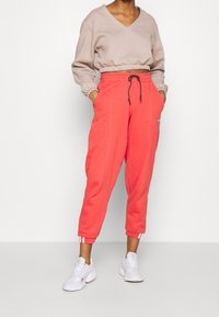 Coral fleece joggers with elastic waistband and drawstring, side pockets, and ribbed cuffs. Paired with a beige V-neck sweatshirt and white sneakers.