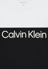 T-shirt noir et blanc à manches courtes, arborant un grand logo "Calvin Klein" en blanc sur la partie noire, fabriqué en mélange de coton.