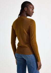 Brun, rippad tröja med en figurnära design, långa ärmar och knappdetaljer vid ärmsluten, tillsammans med blå jeans.
