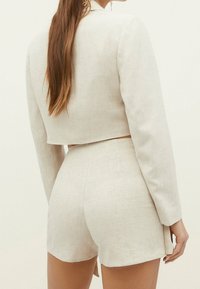 Blazer court en lin beige clair à manches longues associé à un short taille haute assorti. Texture lisse et design minimaliste avec des lignes épurées.