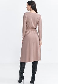 Długie rękawy, mauve sukienka z dopasowaną talią i luźną spódnicą, wykonana z miękkiego materiału. Stylizowana z błyszczącymi czarnymi kozakiem za kolano.