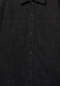 Fekete gombos ing két mellzsebbel és gallérral, a szövet textúráját és a függőleges gombsor elrendezését mutatva.