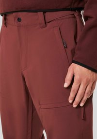 Maroon pants in a soft, smooth fabric with side pockets and detailed stitching. Features a metal button closure at the waistband.