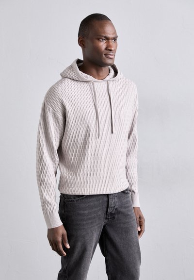 Haut à capuche texturé gris clair avec un motif côtelé, cordons de serrage ajustables et coupe décontractée, associé à un jean gris foncé.