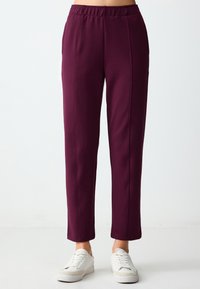Bordeauxrode pull-on broeken met een rechte pijp, met een gladde textuur en contrasterende stiksels. Gepaard met witte sneakers.