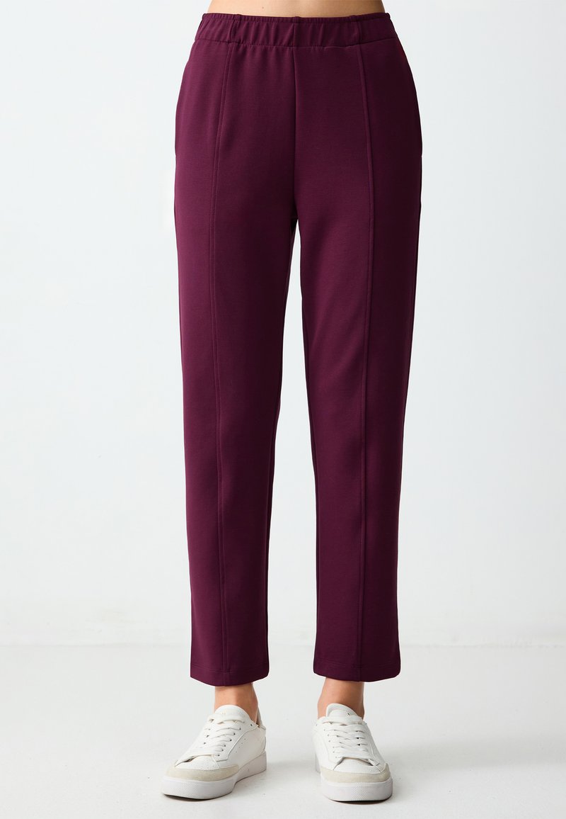 Bordeauxrode pull-on broeken met een rechte pijp, met een gladde textuur en contrasterende stiksels. Gepaard met witte sneakers.
