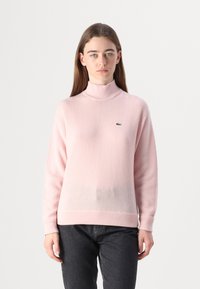 Ljusrosa mock turtleneck-tröja gjord av mjukt tyg, med en liten gr�ön logotyp på bröstet samt ribbade muddar och fåll.