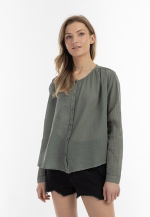 Camicia button-up verde in lino con scollatura rotonda, cuciture delle spalle elasticizzate e maniche lunghe, abbinata a pantaloni corti neri.
