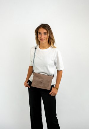 Sac bandoulière marron avec une poche avant transparente, bandoulière bleue réglable, forme rectangulaire et texture lisse. Design minimaliste.