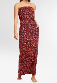 Maxi šaty bez ramínek s tmavě modrým podkladem a vzorem červených listů, elastickým pasem a kapsami po obou stranách. Hladká textura látky.