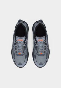 Ζευγάρι γκρι και μαύρα παπούτσια τρεξίματος ASICS με πορτοκαλί λεπτομέρειες λογότυπου, σε θέα από ψηλά σε λευκό φόντο.