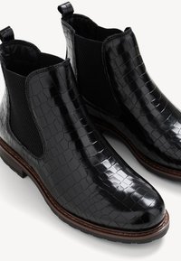 Paire de bottines noires brillantes avec motif crocodile, panneaux latéraux élastiques, languettes de tirage et semelles cousues marron.