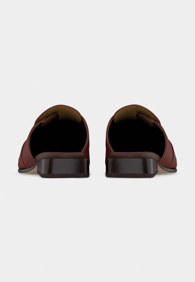 Ζευγάρι καφέ επίπεδων παπουτσιών τύπου slip-on με τετράγωνες φτέρνες, εμφανιζόμενα από πίσω σε ανοιχτό γκρι φόντο.