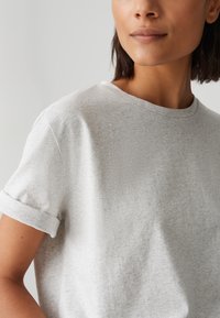 T-shirt en coton gris à col rond et manches courtes repliées. Le tissu a une texture douce et un subtil motif chiné.