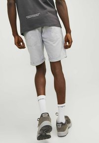 Pantalones cortos de mezclilla gris claro con dobladillos enrollados, combinados con zapatos deportivos grises y calcetas blancas. Diseño sencillo con bolsillos traseros visibles.