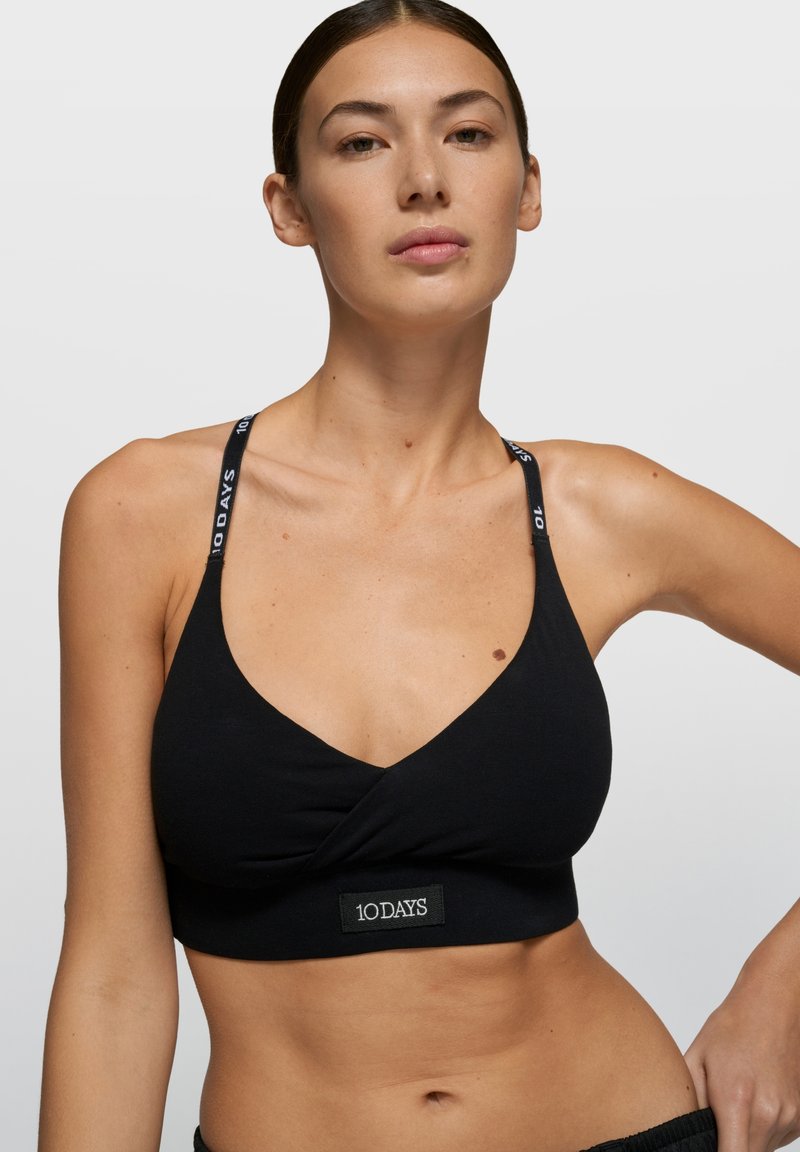 Bralette negro con diseño cruzado, cuenta con tirantes ajustables con detalles de logo. Textura suave de algodón y silueta ajustada.