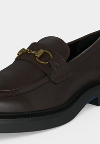 Σκούρο καφέ δερμάτινο loafer με μαύρη σόλα και χρυσή μεταλλική λεπτομέρεια σχήματος αλόγου στην κορυφή.