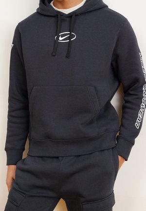 Hoodie gris foncé avec cordons de serrage et poche kangourou ; présente un logo blanc sur la poitrine et du texte sur la manche droite. Texture lisse.