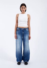 White cropped tank top paired with wide-leg blue denim jeans. The jeans feature a faded wash and five-pocket design. Black shoes complete the outfit.