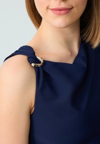 Abito senza maniche blu navy con un design in tessuto attorcigliato sulla spalla, caratterizzato da un accento metallico argentato sulla tracolla. Tessuto morbido.