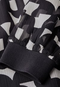 Černobílá vzorovaná tkanina s texturovaným, sklady zdobeným designem a pevným, tkaným černým manžetovým lemem.