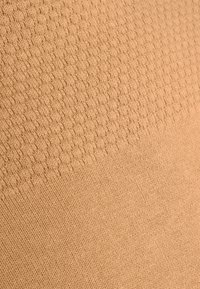 Beige strukturierter Stoff mit einem Wabenmuster an der Oberseite, das sich zu einem glatten Strickstoff am unteren Ende hin verändert. Weiches und leichtes Material.