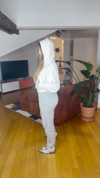 Lys grå hettegenser og joggebukser laget av mykt stoff, med frontlomme og hette. Sølvfargede joggesko fullfører det avslappede antrekket.