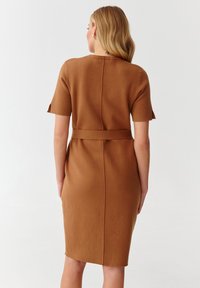 Ruskea, polvipituinen mekko, joka on valmistettu pehmeästä kankaasta. Siinä on lyhyet hihat, vyötäröllä vyö ja keskellä takasaumassa muotoiltu istuvuus.