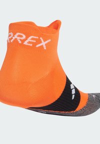Calcetín bajo naranja con acentos en negro y gris. Hecho de material texturizado y transpirable, con letras de la marca en blanco en el puño.