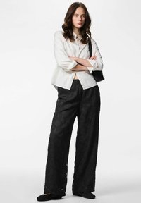 Valge lühendatud lõike ja nööpidega särk, mille juurde on sobitatud mustad laiad püksid lillemustriga. Komplekti kuuluvad must kott ja madalad kingad.