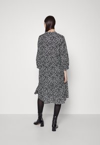 Schwarz-weiß gemustertes Kleid mit langen Ärmeln, knielang und mit einem Rüschensaum. Getragen mit schwarzen Stiefeletten und blickdichten Strumpfhosen.