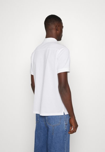 Camisa polo blanca de manga corta con cuello, de corte recto y con aberturas laterales, confeccionada en un tejido suave y texturizado.