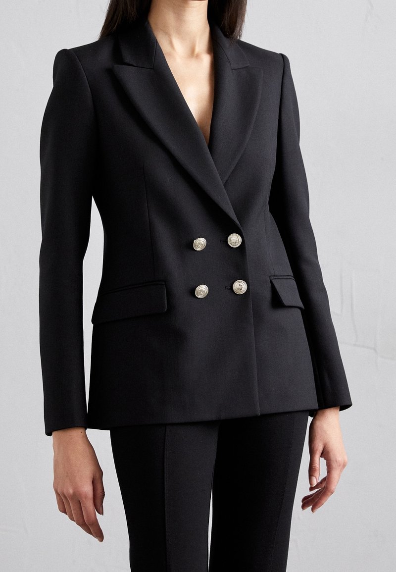 Blazer doppiopetto nero realizzato in tessuto liscio, con rever affilati, bottoni argentati e tasche laterali. Vestibilità sartoriale e design strutturato.
