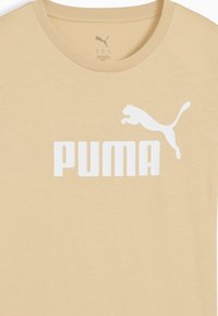 Puma majica u svijetloj bež boji. Okrugli izrez, kratki rukavi, s velikim bijelim "PUMA" logom i siluetom skakanja pume u središtu. Mekani materijal.
