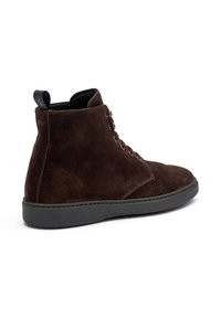 Botas de ante marrón hasta el tobillo con punta redondeada, seis ojales y suela de goma negra. Cuenta con una lengüeta en la parte posterior para ponerlas fácilmente.