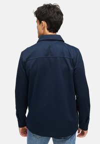 Mørkeblå langærmet skjorte med struktureret krave, tekstureret stof og rygbælte detalje. Parret med jeans.