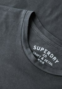 Mørkegrå bomulds T-shirt med rund hals, glat tekstur og et mærke med "Superdry"-branding i hvid.