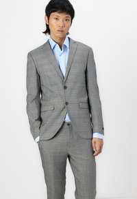 Sivi karirani odijelo slim fit kroja, s dva gumba, reverima i svijetloplavom košuljom ispod. Glatka tekstura tkanine.