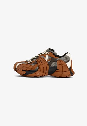 Sneaker med en strukturerad ovandel i brunt och grått nätmaterial, med gummibeläggningar och en framträdande svart sula. Snörning och vadderad krage.