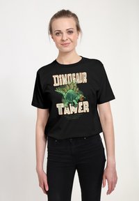 Čern�é tričko s grafickým vyobrazením dinosaura a nápisem "DINOSAUR TAMER" v tučných, barevných písmenech.