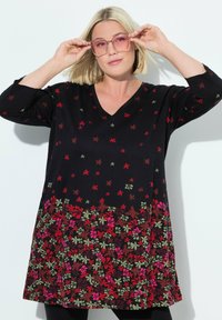 Zwarte tuniek met V-hals, met een bloemenpatroon in rood, groen en roze aan de zoom. Lange mouwen en een relaxte pasvorm.