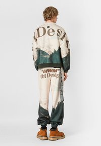 Chándal de corte relajado, estampado en beige y verde con gráficos de montaña. Cuenta con puños holgados, acentos de logo y una práctica cintura con cordón ajustable.